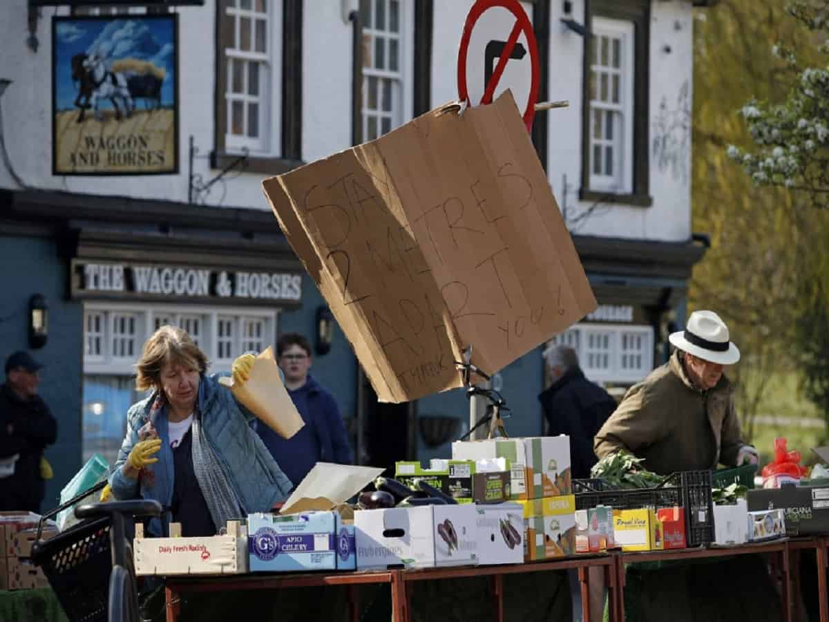 A woman chooses fruit and vegetables as people observe social distancing as they wait in a queue at a fruit and vegetable market in Hartley Wintney, Hampshire on March 28, 2020.