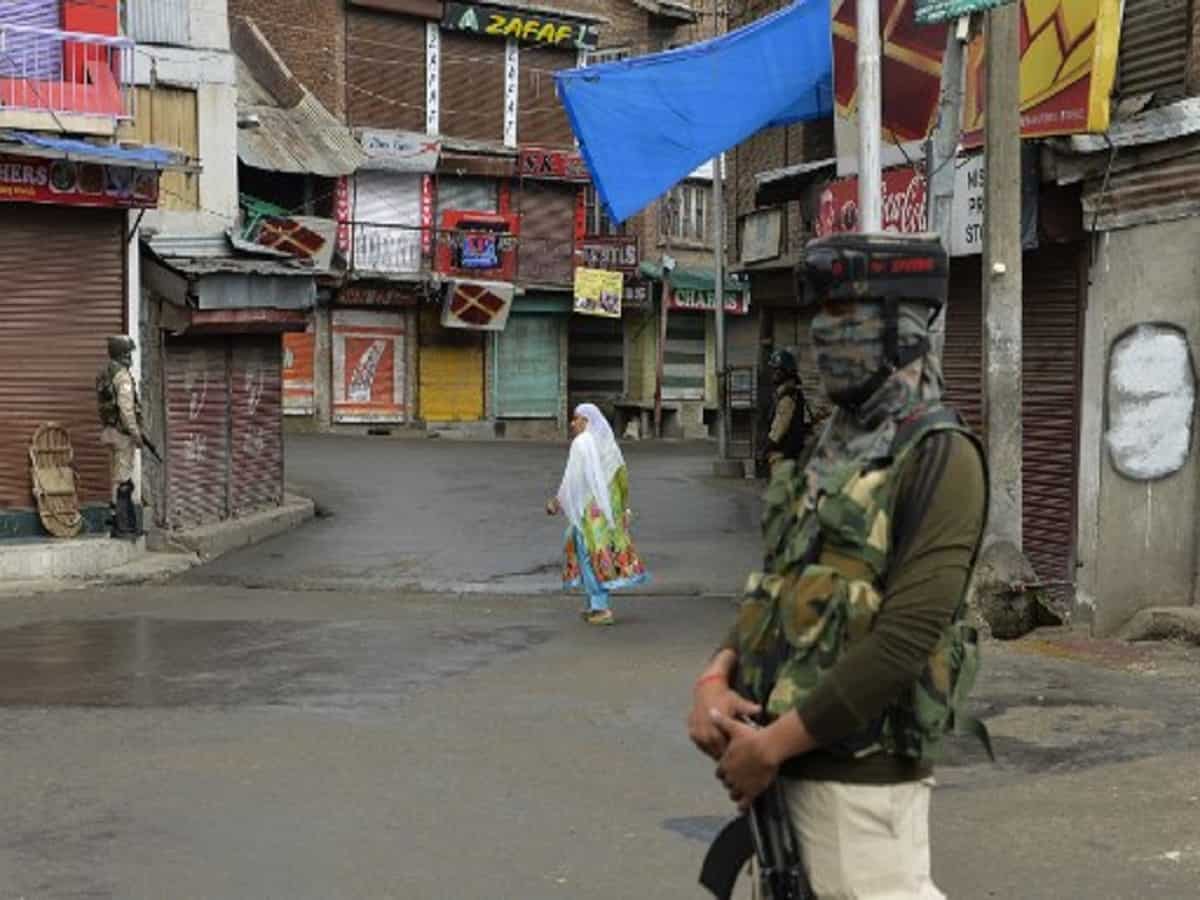 In this picture taken on August 9, 2019 a woman walks past security personnel guarding a street in Srinagar as widespread restrictions on movement and a telecommunications blackout remained in place after the Indian government stripped Jammu and Kashmir of its autonomy. (Photo by Sajjad HUSSAIN / AFP)
