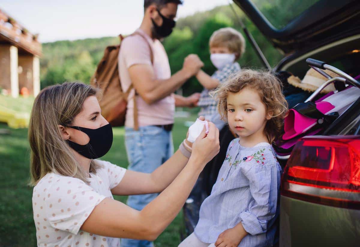 Family with two small children loading car for trip in countryside, wearing face masks
